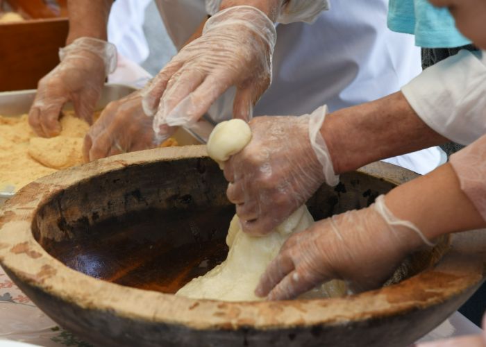 Two sets of gloved hands are kneading mochi in a large stone bowl.